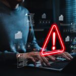 Case Study Cyberangriff: Cyberangriff auf die IT-Infrastruktur eines Unternehmens mit digitalem Warnsymbol am Laptop.
